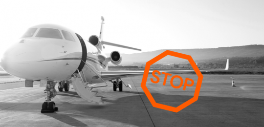 Schwarzweiß-Foto eines Privatjets auf dem Flugfeld, links daneben ein orange-farbenes Stopp-Schild